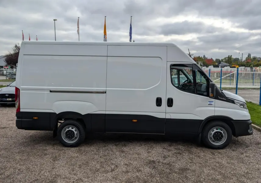 Fourgon Iveco Daily blanc vu de profil côté gauche avec portes coulissantes et protections noires basses.