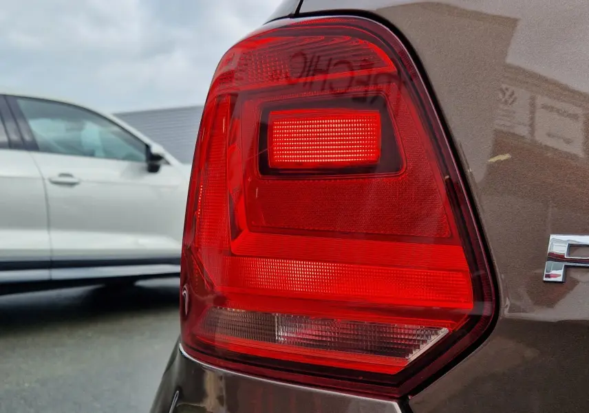 Gros plan sur le feu arrière droit d’une Volkswagen Polo 1.4 TDI brun 2015, finition Lounge, avec reflet du logo VW.