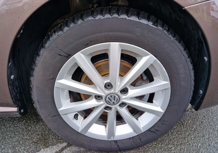 Gros plan sur la roue avant droite avec jante alliage argentée du Volkswagen Polo brun 2015 finition Lounge.