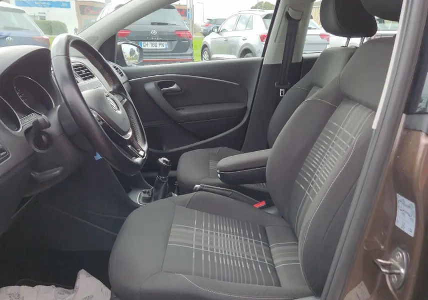Vue intérieure côté conducteur de la Volkswagen Polo 1.4 TDI brun 2015, sièges tissu à motifs et volant cuir multifonction.