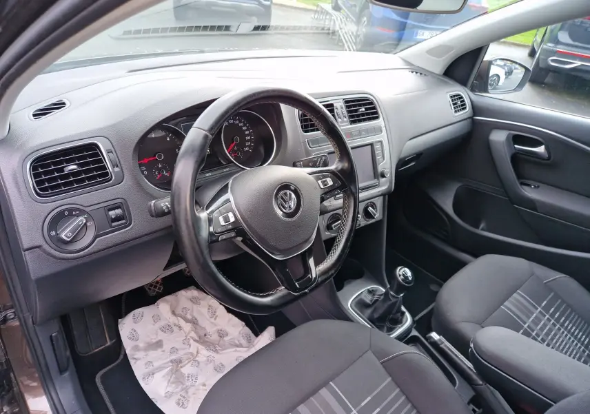 Vue intérieure côté conducteur d'une Volkswagen Polo 2015 finition Lounge, volant cuir multifonctions et boîte manuelle visible.