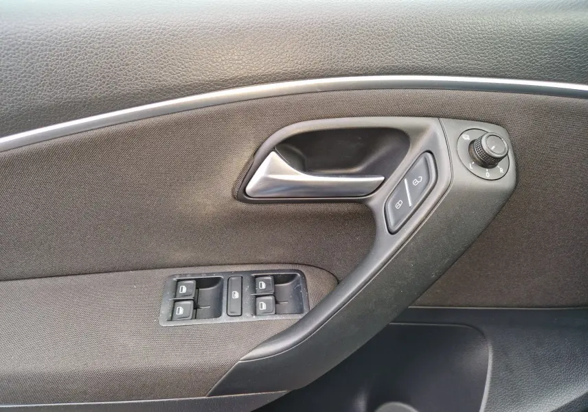Détail de la porte intérieure côté conducteur de Volkswagen Polo 2015 brun, avec commandes de vitres et rétroviseurs électriques.