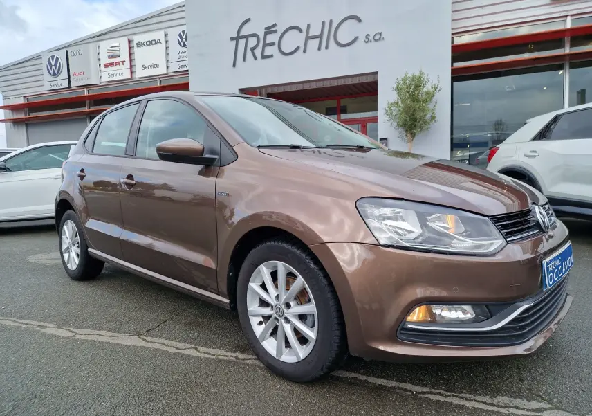 Volkswagen Polo 1.4 TDI brun vue 3/4 avant droit, avec jantes alliage et feux allumés devant un concessionnaire.