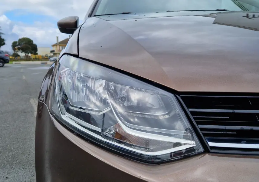 Gros plan sur l'avant gauche d'une Volkswagen Polo 2015 brun métallisé, mettant en valeur son phare et la calandre.