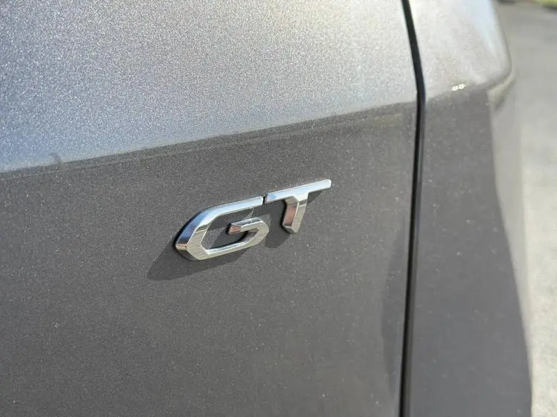 Gros plan sur l'emblème GT en chrome sur la porte gris Platinium d'un Peugeot 3008 2024, version essence.