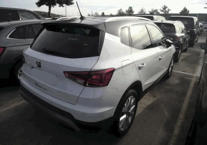 Vue 3/4 arrière droite d'un SEAT Arona blanc Nevada avec toit noir et vitres arrière surteintées, garé en extérieur.