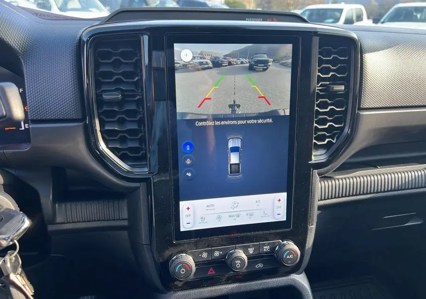 Vue intérieure centrée sur l’écran tactile vertical du Ford Ranger blanc glacier, affichant la caméra de recul et commandes clim.