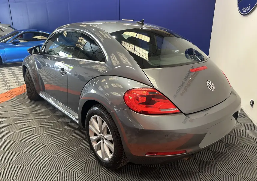 Volkswagen Coccinelle gris vue 3/4 arrière droit, avec feux arrière rouges et jantes alliage en showroom.