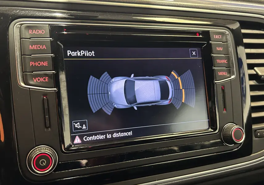 Écran central de la Volkswagen Coccinelle gris montrant l'interface ParkPilot avec alertes de distance au stationnement.