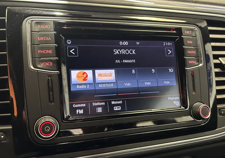 Écran tactile central du tableau de bord de la Volkswagen Coccinelle gris, affichant la radio FM sur Skyrock.