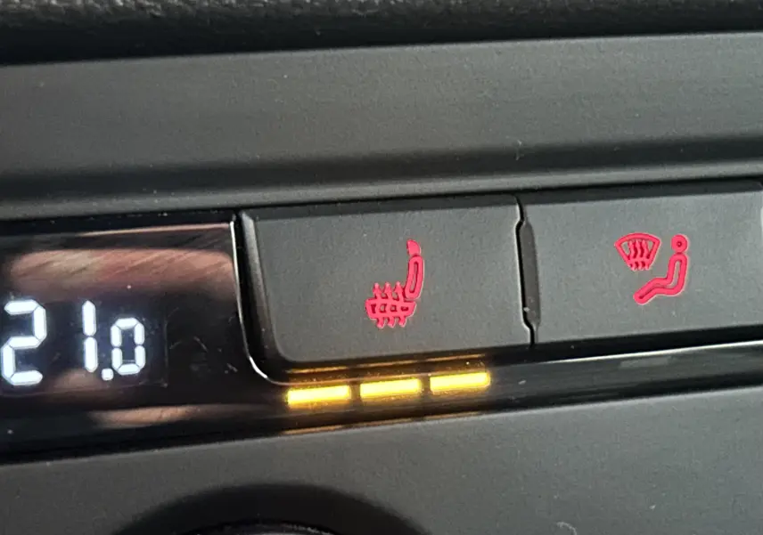 Détail du tableau de bord de la Volkswagen Coccinelle gris, montrant les commandes de siège chauffant et de désembuage activées.