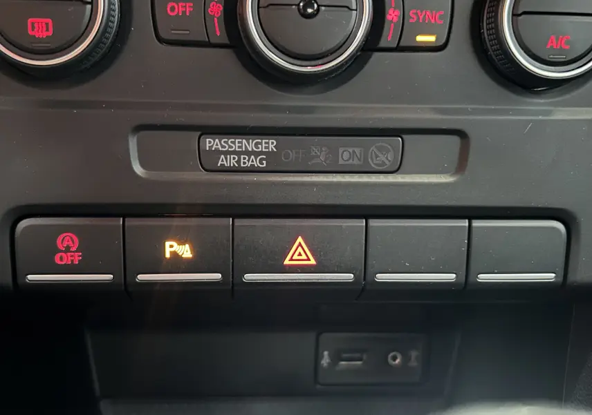 Détail du tableau de bord de la Volkswagen Coccinelle 2016 gris, montrant les commandes climatisation et boutons d’alerte et parking.