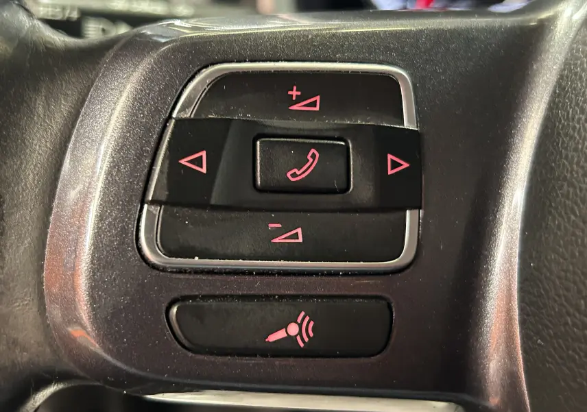 Gros plan sur les commandes au volant noir avec boutons de gestion d’appel et volume éclairés en rouge dans une Volkswagen Coccinelle gris 2016.