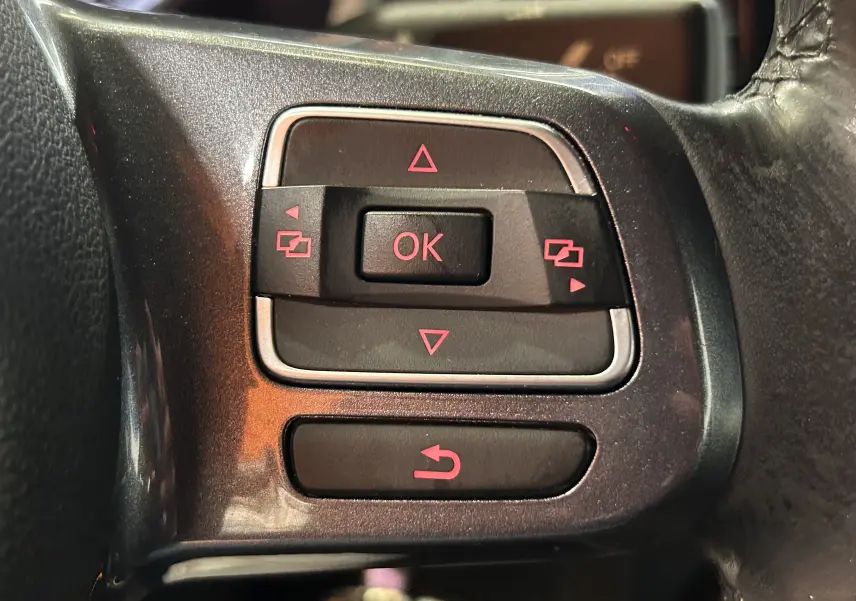 Gros plan sur les commandes multifonctions du volant en cuir gris foncé de la Volkswagen Coccinelle 2016.