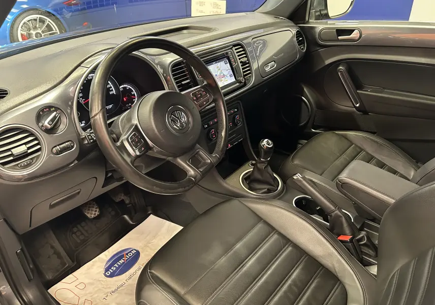 Vue intérieure côté conducteur de la Volkswagen Coccinelle 2016 avec sellerie cuir noire et écran GPS intégré.