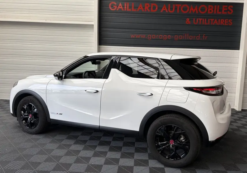 Vue de profil côté gauche d’un DS3 Crossback blanc 2022 avec jantes noires et toit noir, stationné en intérieur.