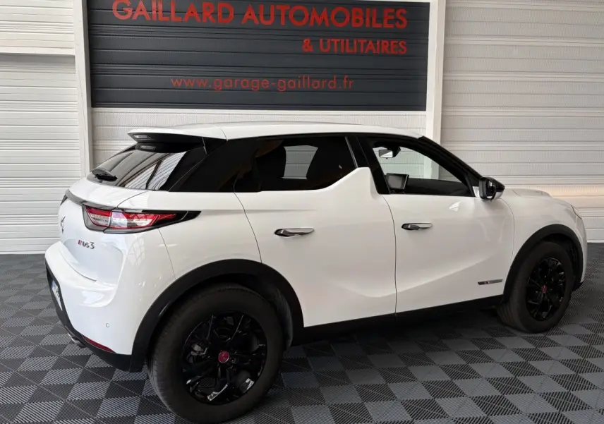 Vue 3/4 arrière droite d'un DS3 Crossback blanc avec toit noir et jantes noires dans un garage.