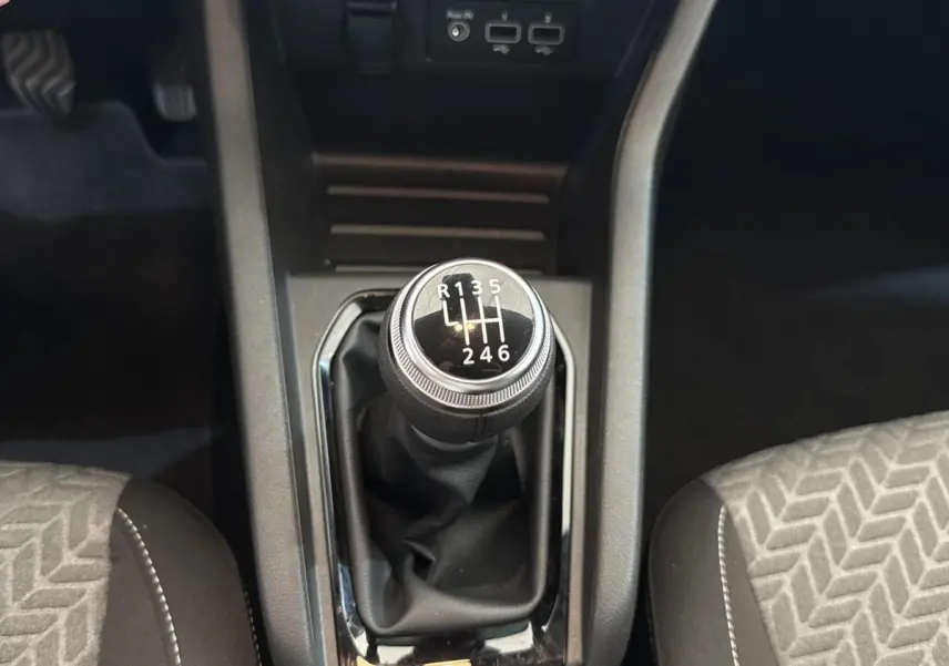 Gros plan sur le levier de vitesses manuel noir entouré de la console centrale et des sièges tissu gris à motifs.