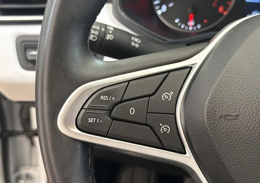 Gros plan sur les commandes du régulateur de vitesse au volant noir de la Renault Clio blanche 2023.