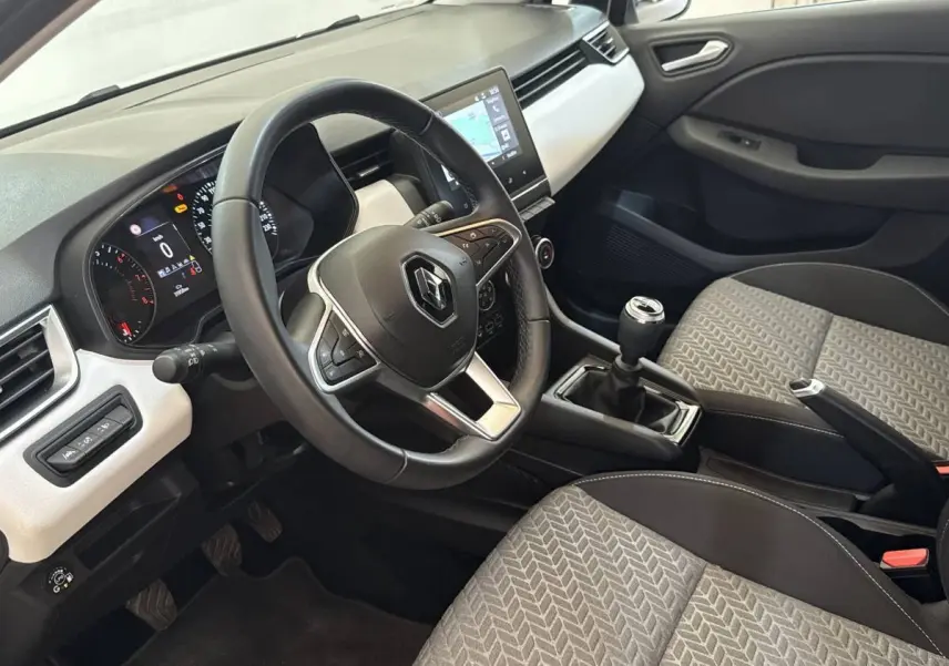Vue intérieure côté conducteur de la Renault Clio blanche 2023, volant cuir, écran tactile central et levier de vitesse manuel.
