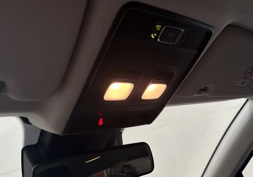 Plafonnier intérieur allumé vu de dessous avec miroir de courtoisie et panneau de commande noir dans une Renault Clio blanche.