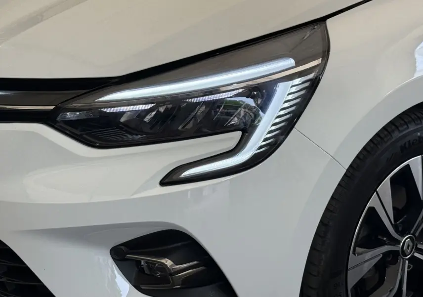 Gros plan sur le phare avant droit allumé d’une Renault Clio blanche Evolution TCe 100 GPL 2023.
