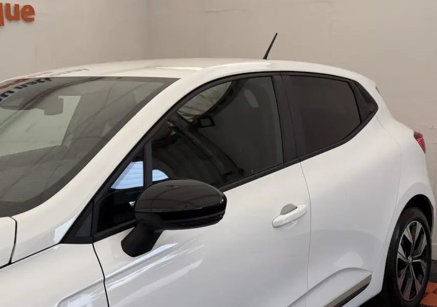 Vue latérale droite d'une Renault Clio blanche 2023 avec rétroviseur noir et vitres teintées.