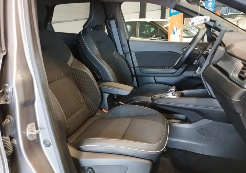 Vue intérieure côté conducteur de la Renault SYMBIOZ 1.6 E-Tech Hybride 2025 en gris Cassiopée, sièges noirs avec surpiqûres blanches.