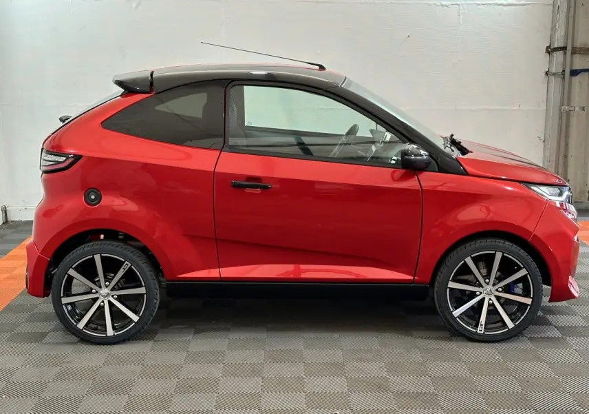 Vue de profil droit de l'AIXAM AMBITION 0.5 CITY COUPE GTI E5+ rouge avec toit noir et jantes alliage distinctives.