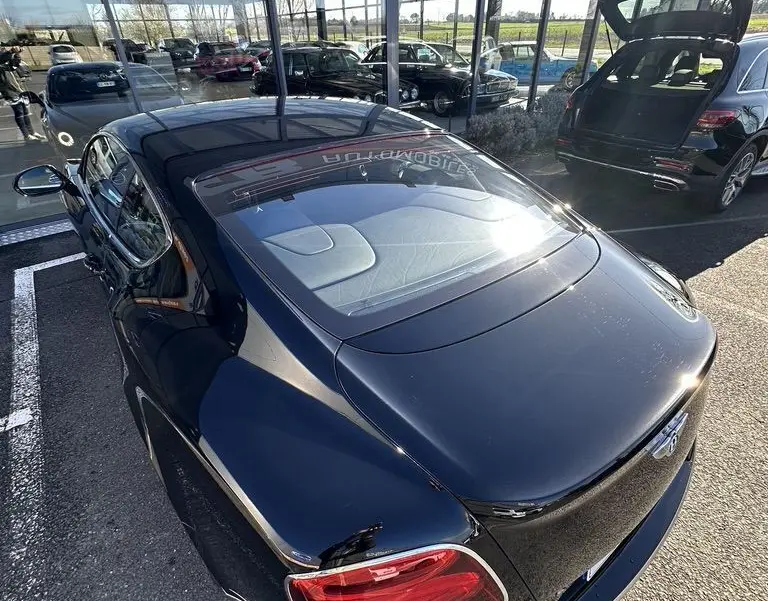 Vue 3/4 arrière haute d'une Bentley Continental GT Speed noire brillante avec feux arrière rouges et toit vitré.