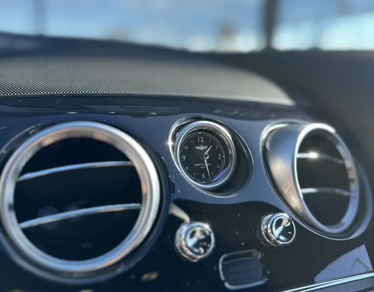 Gros plan sur l'horloge Breitling et les aérateurs chromés du tableau de bord noir d'une Bentley Continental GT Speed 2015.