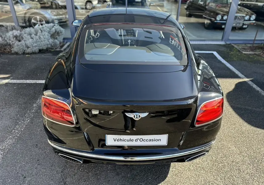 Vue arrière d'une Bentley Continental GT Speed noire de 2015 avec feux rouges et double sortie d'échappement chromée.