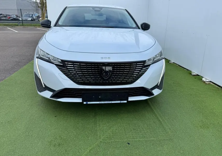 Vue frontale d'une Peugeot 308 SW blanche Okenite avec calandre noire et feux LED verticaux distinctifs.