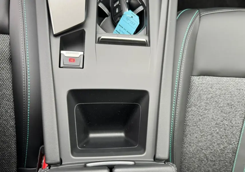 Gros plan sur la console centrale et accoudoir avant en sellerie noire avec surpiqûres bleues du Peugeot 308 SW blanc Okenite 2024