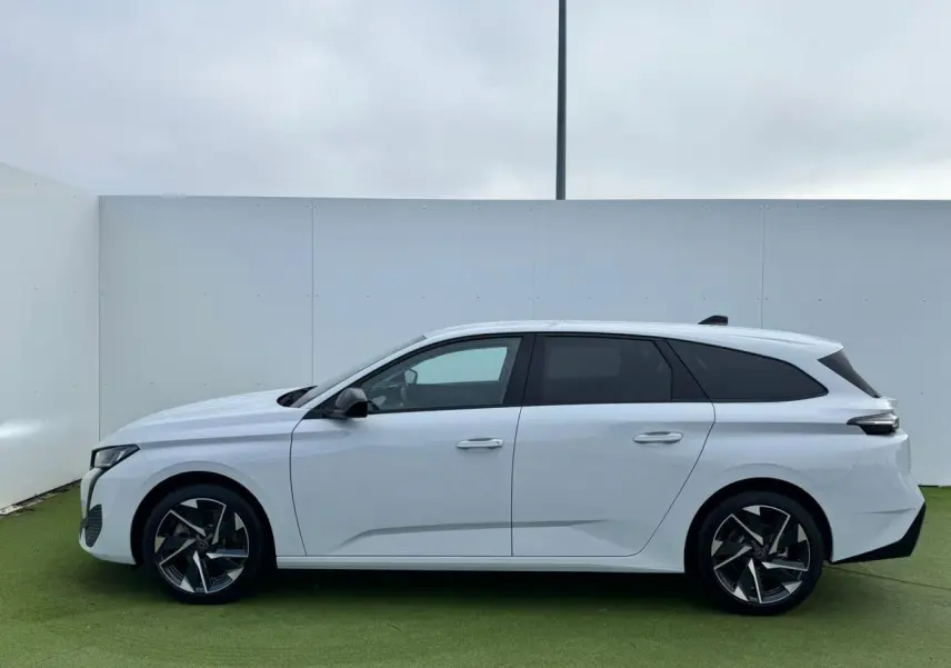 Profil latéral droit d'une Peugeot 308 SW 2024 blanche Okenite avec jantes alliage 17'' Halong diamantées et vitres surteintées.