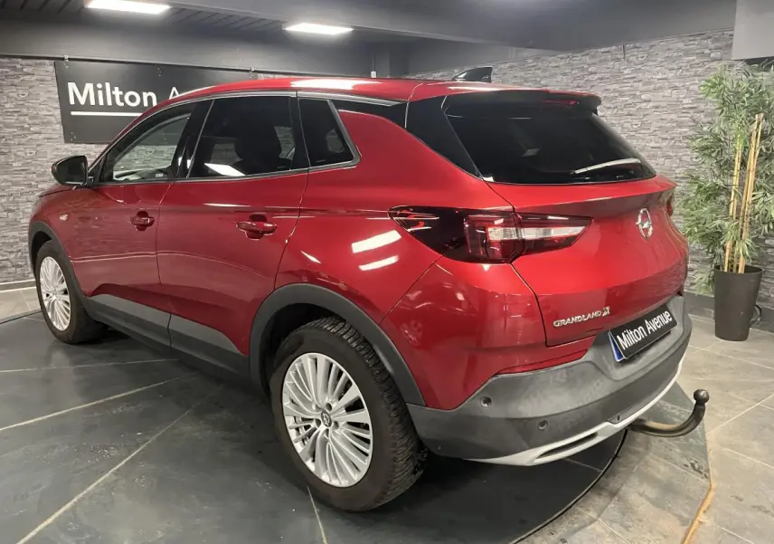 Opel Grandland rouge métallisé vue 3/4 arrière droit avec crochet d'attelage amovible en intérieur showroom.