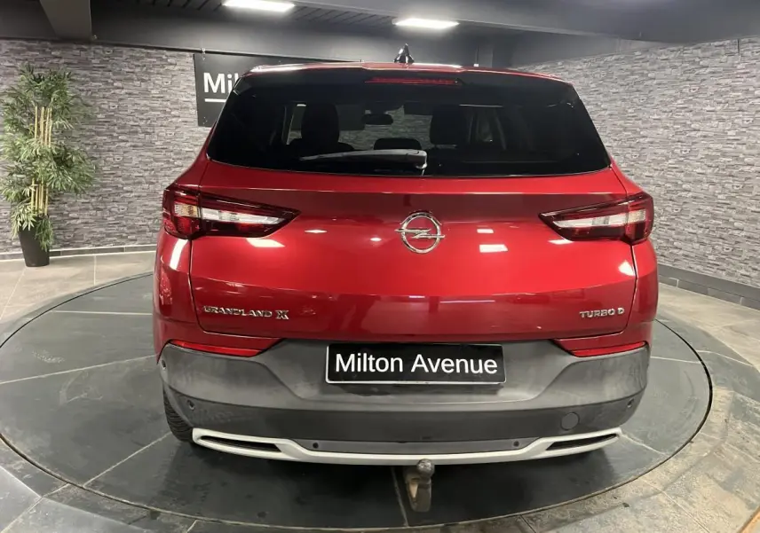 Vue arrière d'un Opel Grandland X rouge métallisé avec crochet d'attelage dans un showroom intérieur.