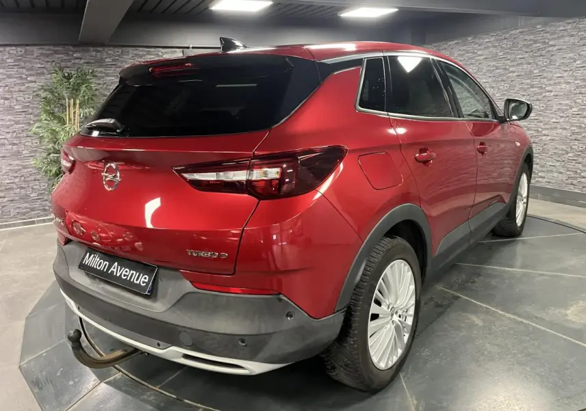 Opel Grandland rouge métallisé en 3/4 arrière droit avec crochet d'attelage amovible visible dans un showroom.
