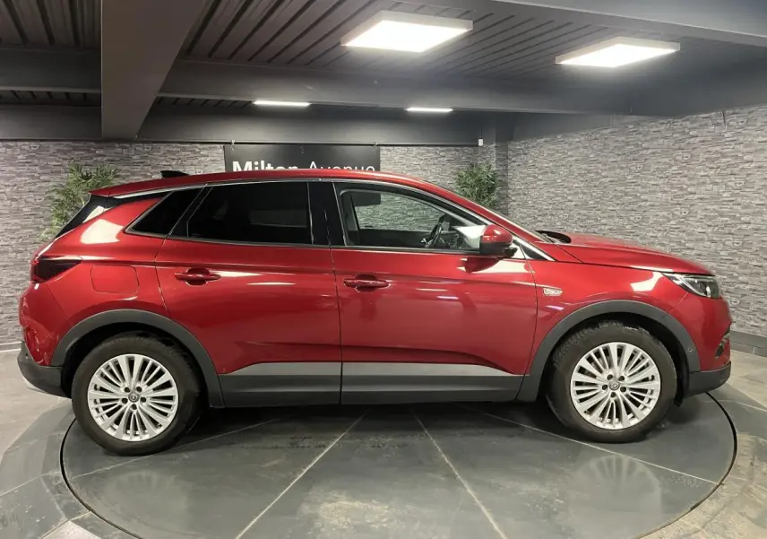 Opel Grandland rouge métallisé vu de profil côté gauche dans un showroom avec jantes alliage 18 pouces.