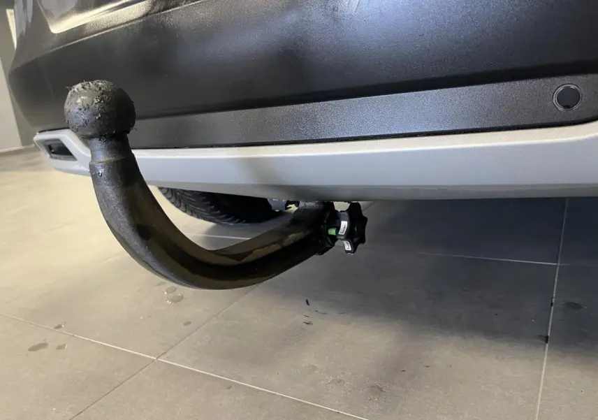 Gros plan sur le crochet d'attelage amovible noir sous le pare-chocs arrière gris d'un Opel Grandland rouge.