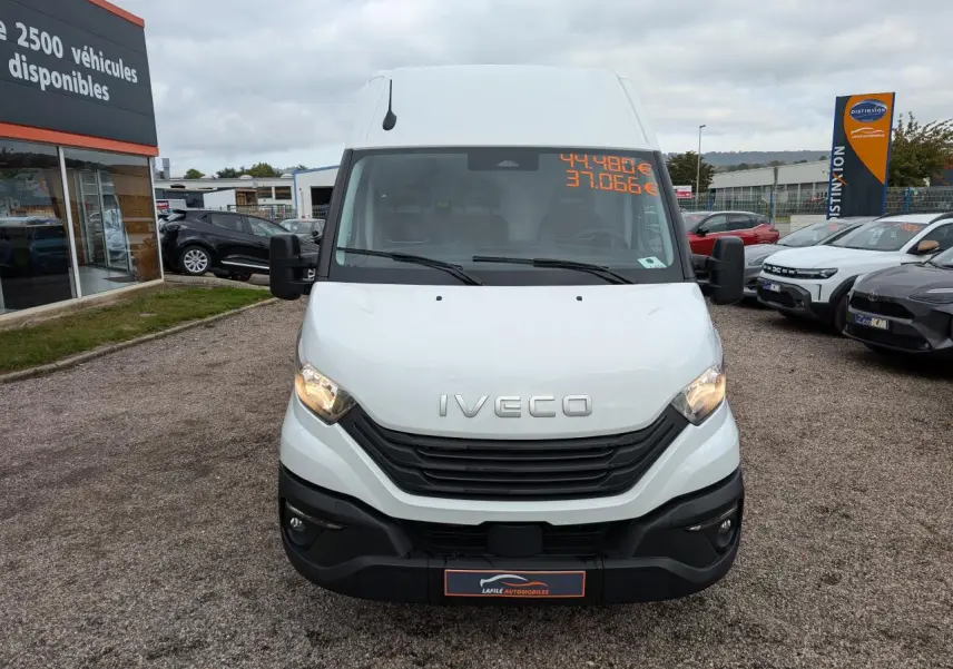 Vue de face d'un utilitaire Iveco Daily blanc avec calandre noire et phares allumés sur un parking.