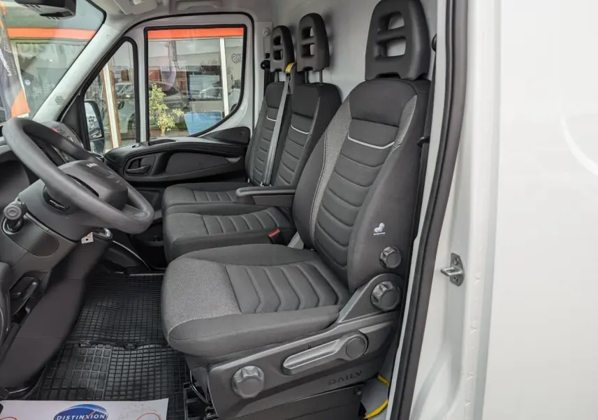 Intérieur côté conducteur du fourgon Iveco Daily blanc 2025, montrant les sièges en tissu gris et le tableau de bord noir.