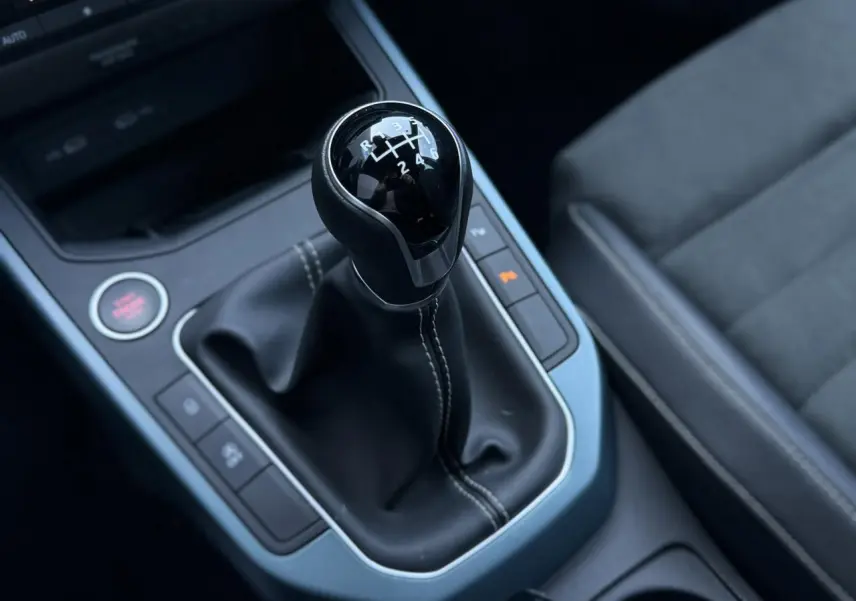 Gros plan sur le levier de vitesse manuel noir avec coutures blanches et sellerie suédine grise du SEAT Arona TSI 115 Xpérience.