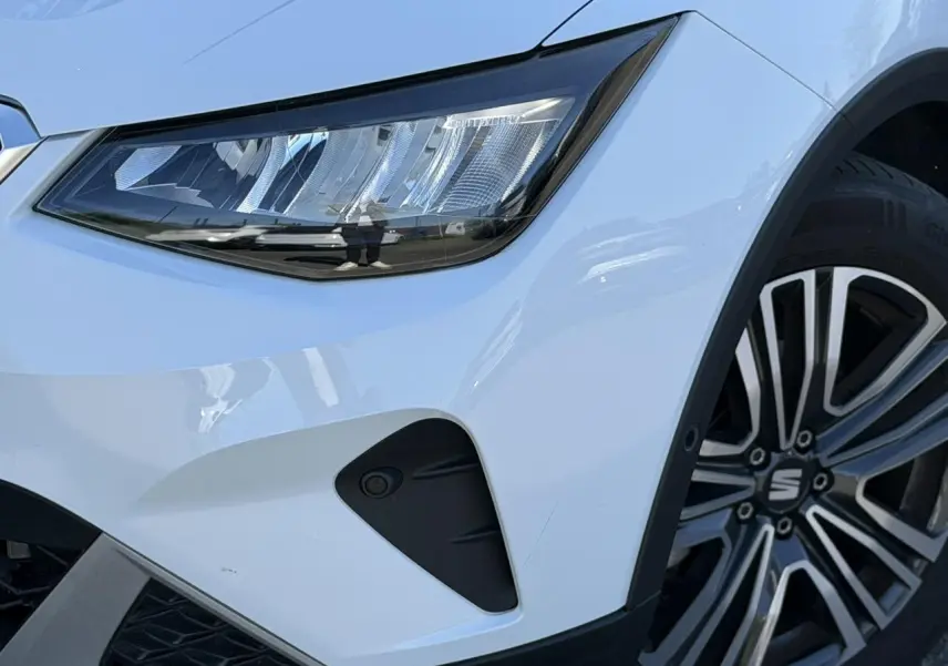 Gros plan sur l'avant droit du SEAT Arona blanc Nevada, mettant en valeur le phare LED et la jante alliage 17 pouces.