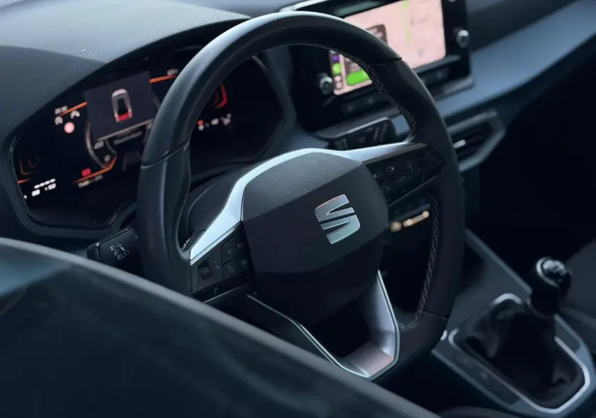 Vue intérieure centrée sur le volant multifonction de la SEAT Arona avec tableau de bord digital et levier de vitesse manuel.