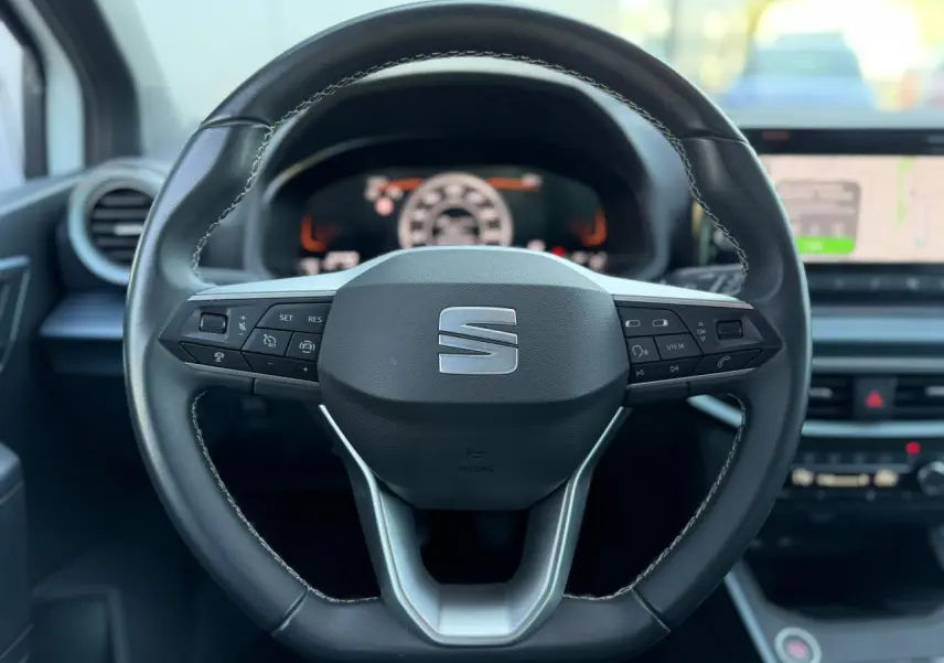 Vue rapprochée du volant cuir noir du SEAT Arona 2025 avec commandes intégrées et tableau de bord digital flou en arrière-plan.