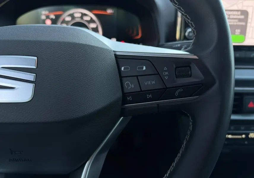 Gros plan sur le côté droit du volant noir du SEAT Arona avec commandes multifonctions et tableau de bord digital en arrière-plan.