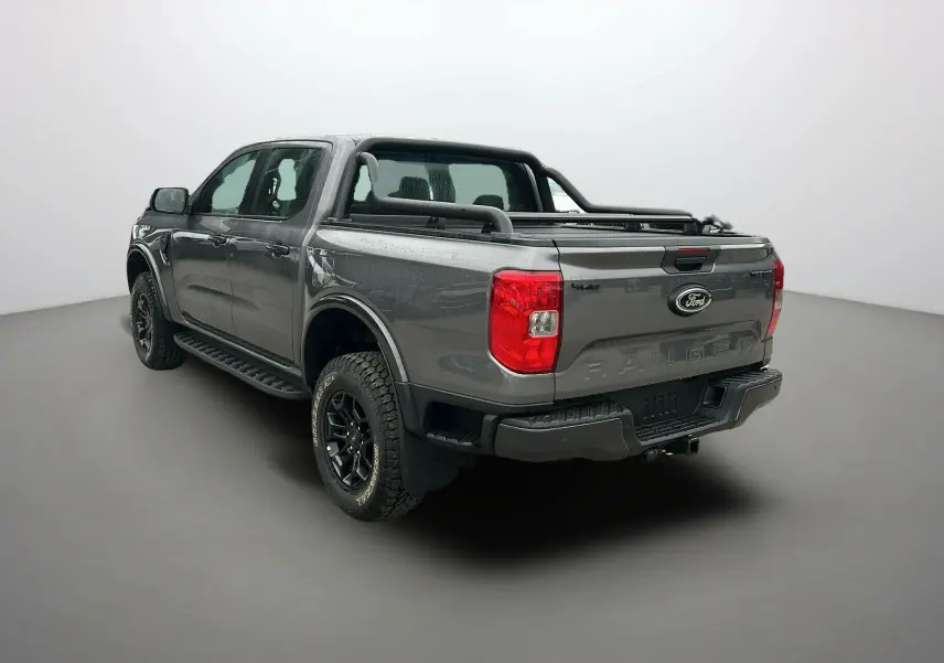 Ford Ranger gris carbone en 3/4 arrière droit, avec arceaux noirs et attelage visible sur la benne.