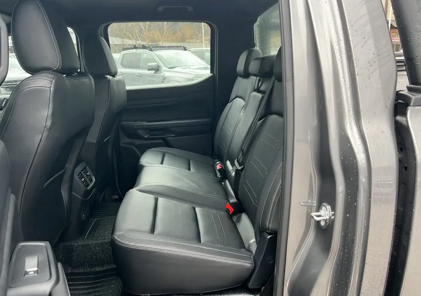 Vue latérale droite de l'intérieur arrière du Ford Ranger 2025 gris carbone avec sièges en cuir noir et ceintures visibles.