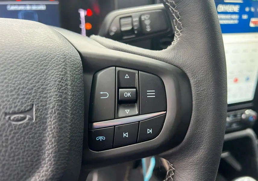 Gros plan sur le volant cuir multifonctions du Ford Ranger 2025, avec commandes audio et écran tactile en arrière-plan.